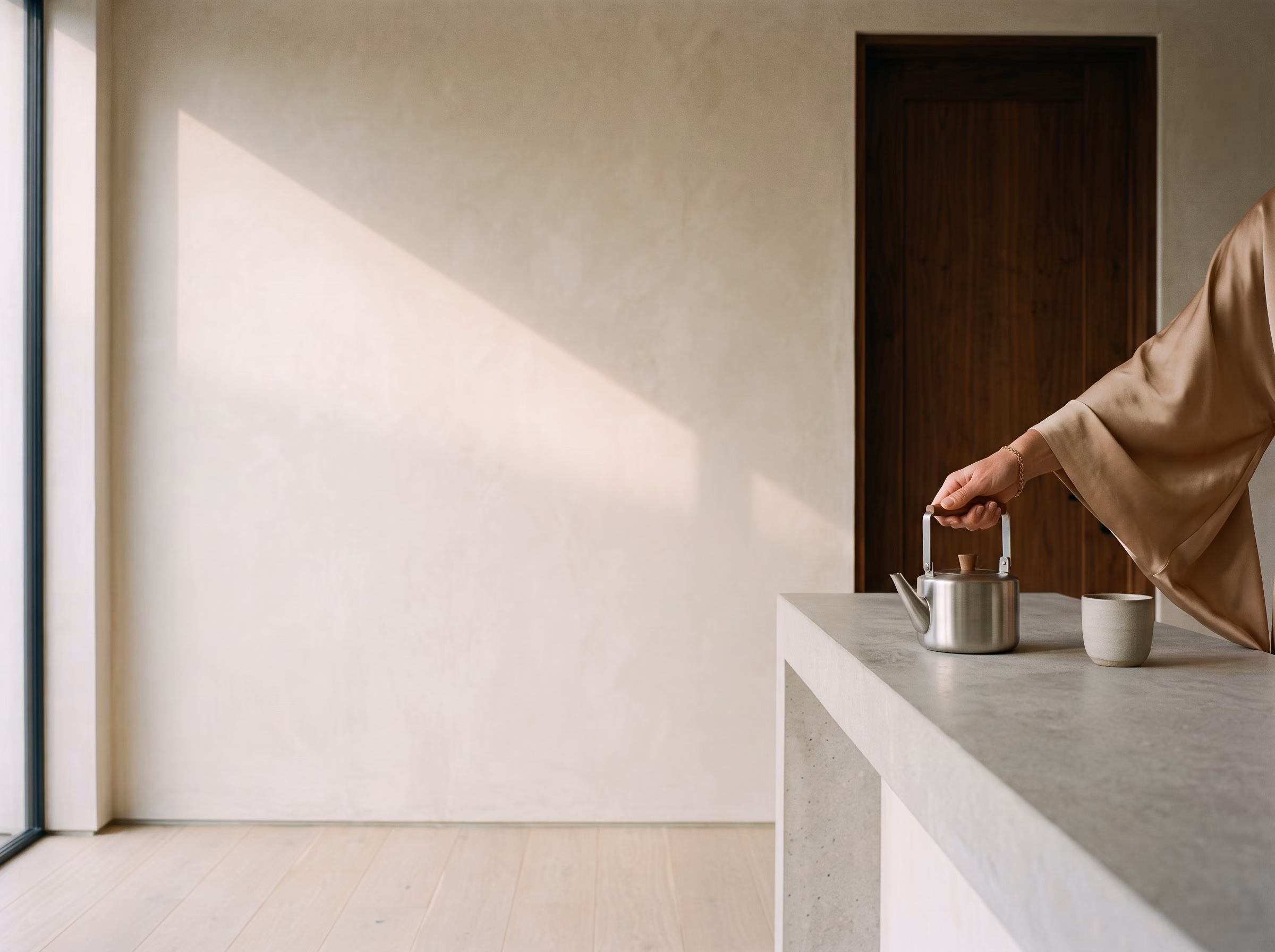 An almond silk sleeve enters the frame. A kettle, a cup, a door standing half open.