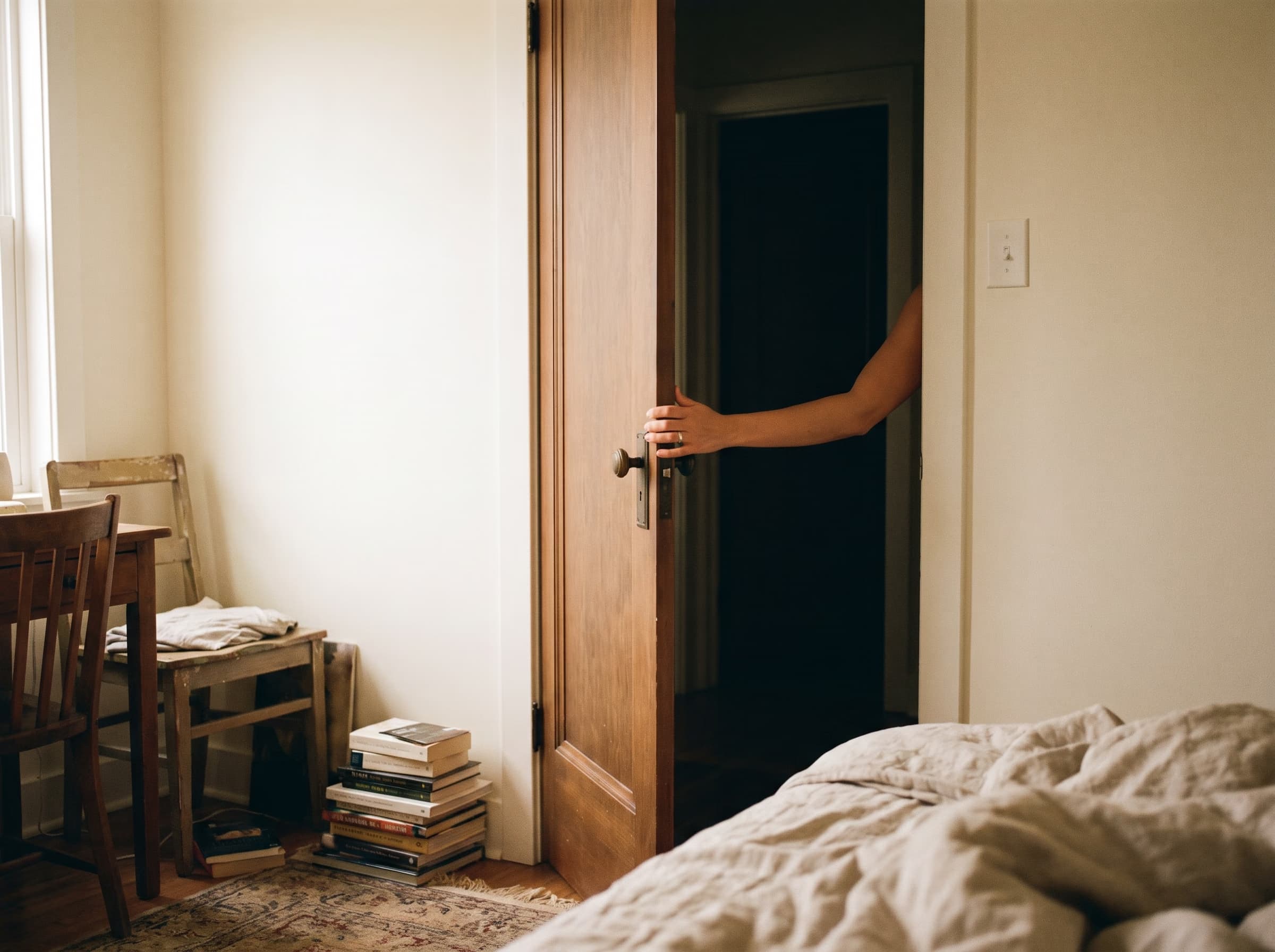 A hand pushes the bedroom door closed. The hallway stays in shadow.